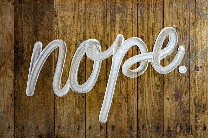 the word "nope" painted on a wooden background -- As an entrepreneur, learning to say "no" and setting boundaries is essential for maintaining both your mental and physical health!